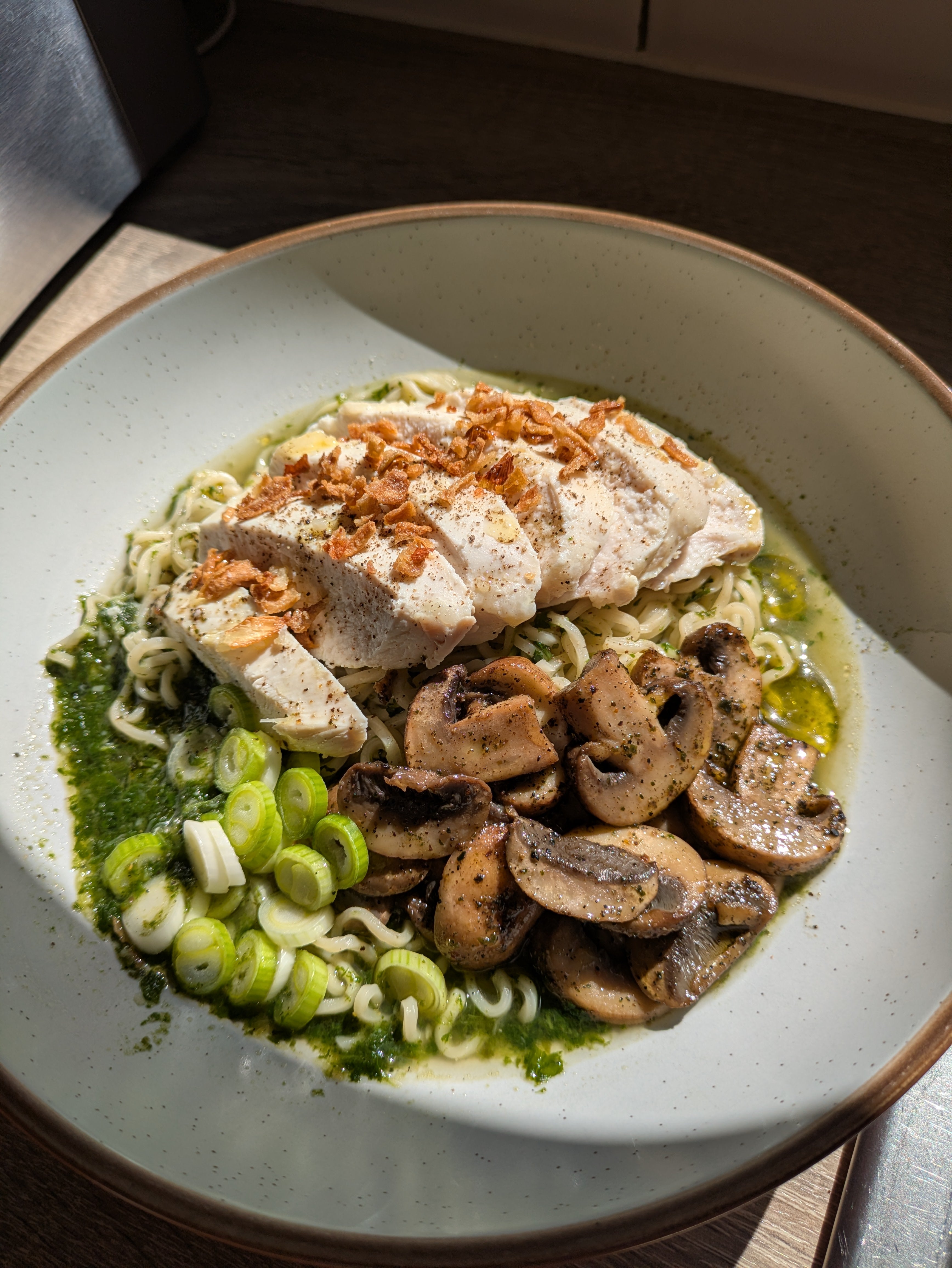 Umami chicken and mushroom noodles in a bowl with spinach, sliced chicken, and garnished with scallions and crispy onions