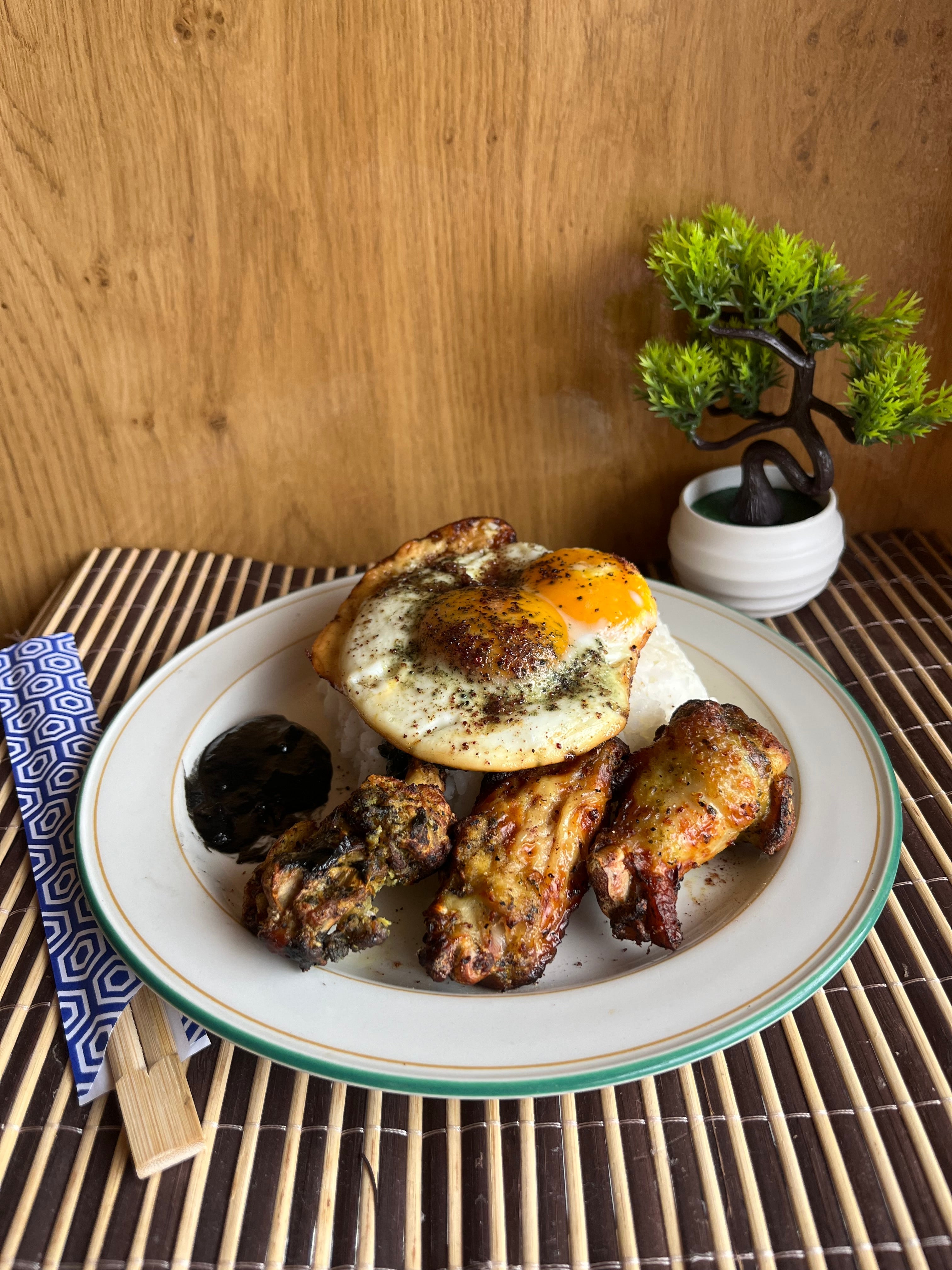 Crispy chicken wings served with rice topped with a fried egg, sprinkled with red kraut seasoning, and black garlic sauce on the side.